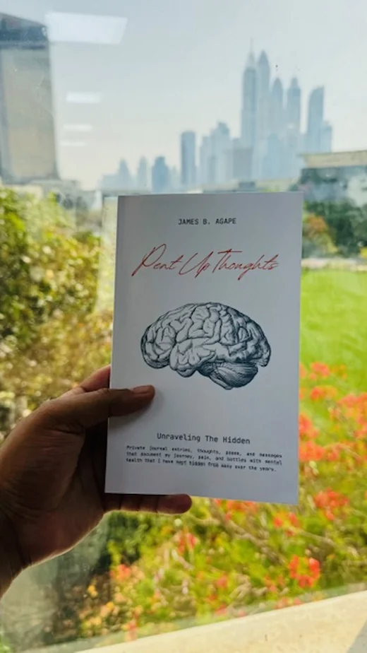 Reader holding Pent Up Thoughts poetry collection by James B. Agape on a balcony overlooking the city