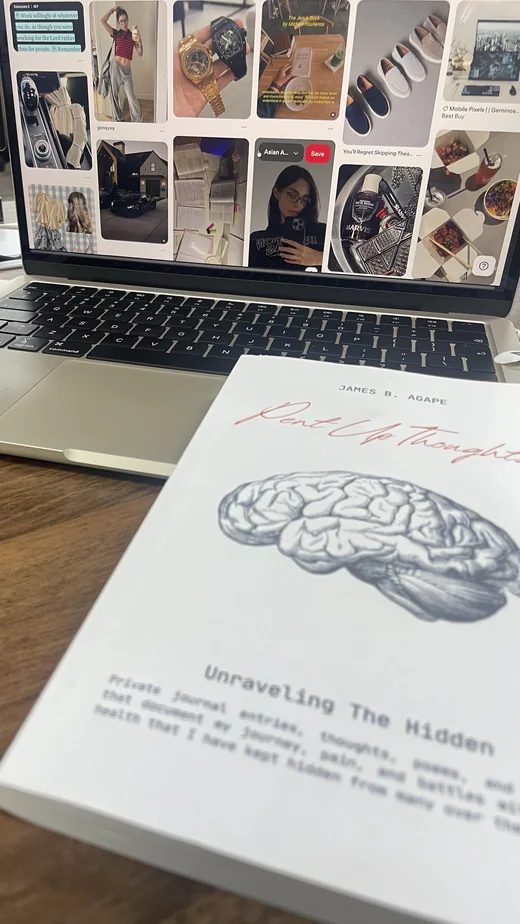 Reader's desk with Pent Up Thoughts poetry collection by James B. Agape and a Pinterest mood board